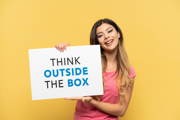 Fototapeta na wymiar Young Russian girl isolated on yellow background holding a placard with text Think Outside The Box with happy expression