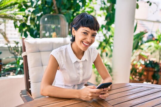 Beautiful woman with short hair sitting at the terrace on a sunny day using smartphone