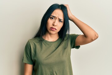 Young hispanic girl wearing casual t shirt confuse and wonder about question. uncertain with doubt, thinking with hand on head. pensive concept.