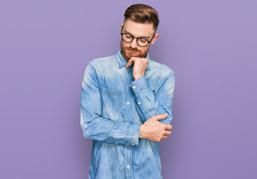 Young redhead man wearing casual denim shirt thinking looking tired and bored with depression problems with crossed arms.