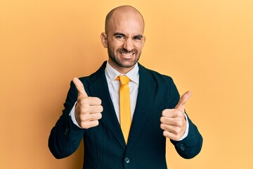 Young hispanic man wearing business suit and tie approving doing positive gesture with hand, thumbs up smiling and happy for success. winner gesture.