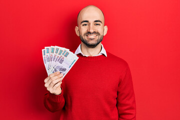 Young bald man holding egyptian pounds banknotes looking positive and happy standing and smiling with a confident smile showing teeth