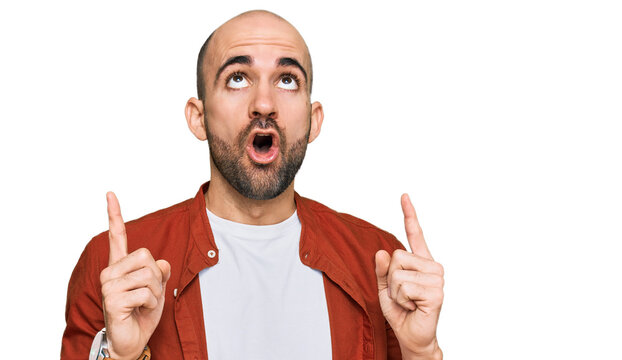 Young hispanic man wearing casual clothes amazed and surprised looking up and pointing with fingers and raised arms.