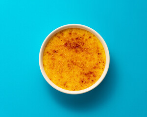 Creme brulee in ramekin isolated on bright blue color background. Close up french dessert. Burned cream. Spanish crema catalana. Top view