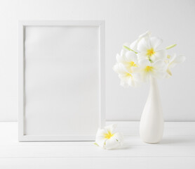 Mock up portrait frame and beautiful Frangipani spa flower in modern ceramic white vase on wooden table white wall background