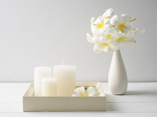 White candles  on white wood  tray and beautiful Plumeria flowers in modern glass vase  composition over white wooden table room interior