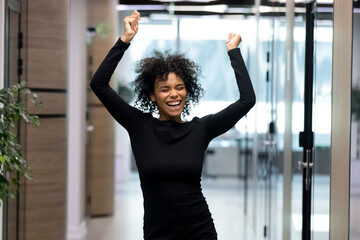 Overjoyed young African American female employee or worker dance in office hallway enjoy Friday...
