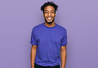 Young african american man with beard wearing casual purple t shirt with a happy and cool smile on...
