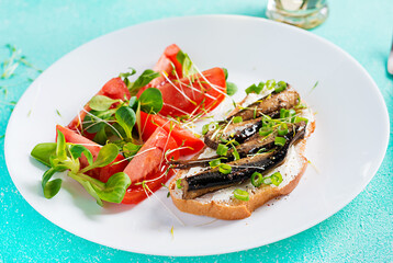 Sandwich - smorrebrod with sprats and tomatoes salad on white plate. Danish cuisine.