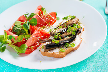 Sandwich - smorrebrod with sprats and tomatoes salad on white plate. Danish cuisine.