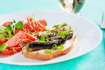 Sandwich - smorrebrod with sprats and tomatoes salad on white plate. Danish cuisine.