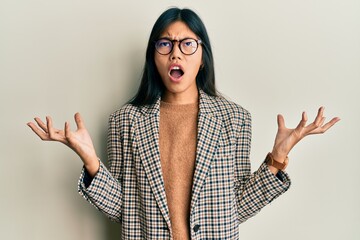 Young chinese woman wearing business style and glasses crazy and mad shouting and yelling with...