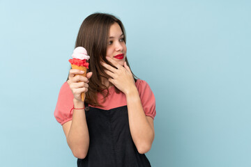 Teenager girl holding a cornet ice cream isolated on blue background thinking an idea and looking side