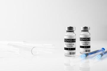 Coronavirus vaccination concept. Medical syringes, and two vials of the COVID-19 vaccine for two-stage injection on a white glass table. Space for text