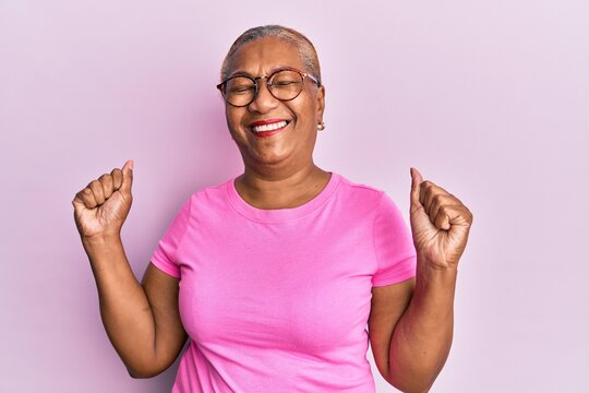 Senior african american woman wearing casual clothes and glasses very happy and excited doing winner gesture with arms raised, smiling and screaming for success. celebration concept.