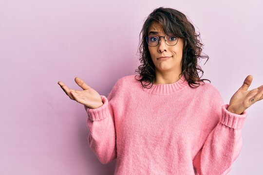 Young hispanic woman wearing casual clothes and glasses clueless and confused with open arms, no idea and doubtful face.