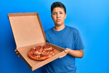 Teenager hispanic boy eating tasty pepperoni pizza looking at the camera blowing a kiss being lovely and sexy. love expression.