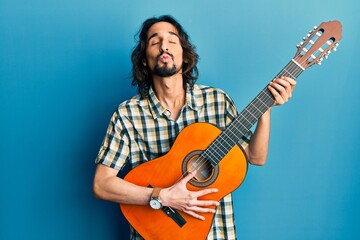 Obraz premium Young hispanic man playing classical guitar looking at the camera blowing a kiss being lovely and sexy. love expression.