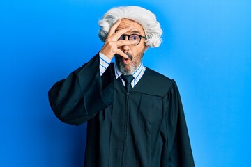 Middle age hispanic man wearing judge uniform peeking in shock covering face and eyes with hand,...