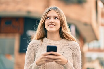 Beautiful caucasian teenager smiling happy using smartphone at the city.