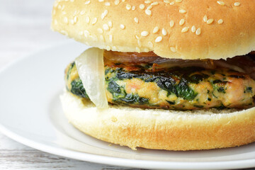 Homemade meat burger with vegetables, spinach. Served on a small white plate, wooden base.