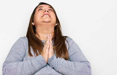 Beautiful brunette plus size woman wearing casual clothes begging and praying with hands together...