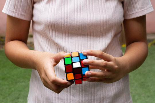 SAMUT-SAKHON, THAILAND - APRIL 04, 2021 : Hands of a young girl trying to solve the Rubik's Cube puzzle on the grass field.