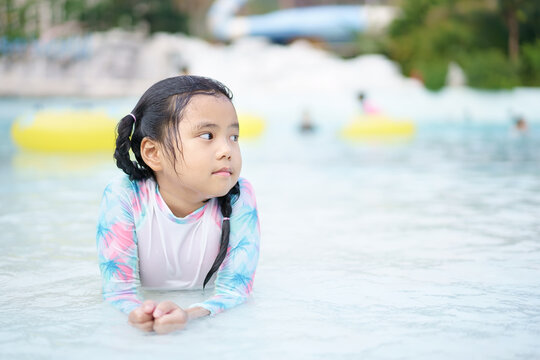 Asian child cute or kid girl wearing swimsuit and lie down sleep to relax on edge swimming pool and smile with happy fun in water park for learn swim and exercise on summer holiday vacation to travel