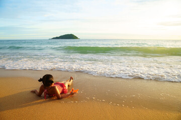 asian child happy or kid girl sit or sleep lie down on sand beach or blue sea with golden warm sunlight on morning sunrise or sunset for vacation travel play on summer holiday relax and wearing bikini