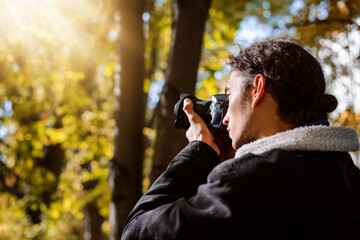Young man taking pictures in the Autumn park. Photographer shooting fall landscapes