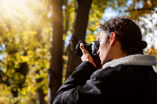 Young man taking pictures in the Autumn park. Photographer shooting fall landscapes