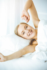 Obraz na płótnie Canvas Happy woman stretching hands in bed after waking up, entering a day happy and relaxed after good night sleep. Sweet dreams, sunny morning concept