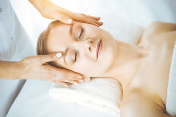 Happy woman enjoying facial massage with closed eyes in spa salon. Relaxing treatment in medicine and Beauty concept