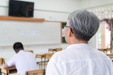 Obraz premium Behind Asian teacher looking all students highschool in exam testroom while thai uniform students concentration testing admission in school rows chairs at classroom in Thailand, Back to school