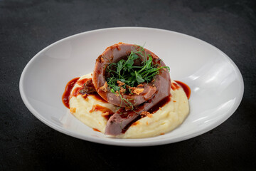 Baked beef tongue with mashed potatoes and sauce on a white plate. British cuisine