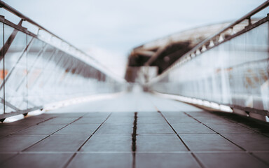 View of a long bright overhead passage or a pedestrian bridge stretching into the distance, glass walls and chrome banister, shallow depth of field with selective focus on the foreground tiles