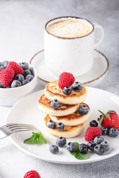 Stack of cheese pancakes with fresh berries, cup of coffee on the table. Tasty breakfast food. Vertical photo - Image
