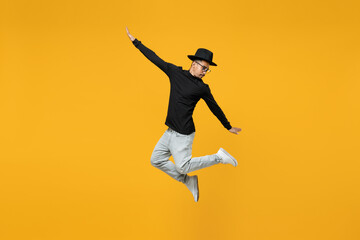 Fototapeta na wymiar Full length of young active fashionable overjoyed fun happy excited african man in stylish black hat shirt eyeglasses jump high with outstretched hands isolated on yellow background studio portrait