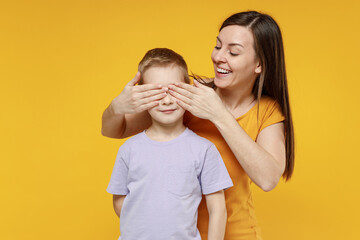 Happy young woman have fun with child baby boy 5-6-7 years old in violet tshirt Mommy little kid son close eyes with hands play guess who isolated on yellow background studio Mother's Day love family
