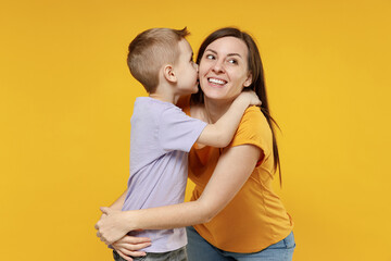 Woman have fun child baby boy 5-6-7 years old age in violet t-shirt whispering tells secret behind hand sharing news Mommy little kid son isolated on yellow background studio Mother's Day love family