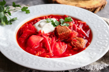 Red borsch with vegetables and meat in a white plate. Tomato soup. Dark background. Delicious healthy lunch. Close up