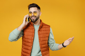 Young smiling friendly fun man 20s wearing orange vest mint sweatshirt glasses talking on mobile...
