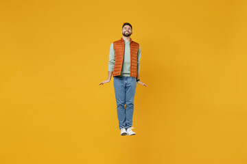 Fototapeta na wymiar Full length young smiling happy cheerful fun man 20s years old wearing orange vest mint sweatshirt jumping high looking camera isolated on yellow background studio portrait. People lifestyle concept.