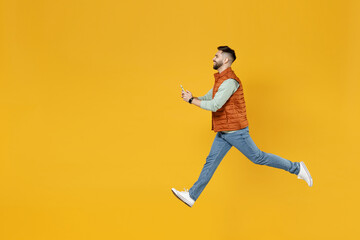 Full length side view young strong powerful fun caucasian man 20s year old in orange vest mint sweatshirt jumping high hold mobile cell phone chat online isolated on yellow background studio portrait