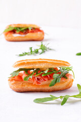 Eclair with salted trout, cream cheese and arugula on the white table
