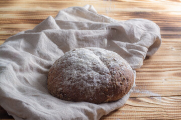 Fototapeta na wymiar Dark rye grain bread with round shape on beige napkin and wooden natural background
