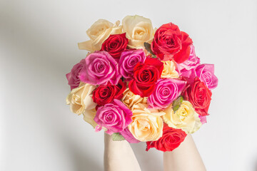 The woman's hands are holding a beautiful bouquet of fresh multicolored roses