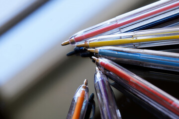 Obraz premium A multitude of translucent, multi-colored ballpoint pens lie on a reflective surface. Concept for creativity, office work, school or college. Macro. Selective focusing