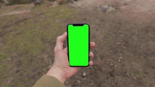 Man hand holding iPhone 11 in vertical or portrait orientation. Tourist walking in the forest near lake. Pre-Keyed green screen ready for your content. POV, point of view. Colorado, USA