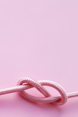 Vertical pastel pink background picture with a rope. A concept for tying the knot, marriage and wedding